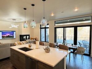 A modern kitchen with a large island, pendant lights, and a dining area with chairs and a table.