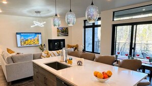 Une cuisine moderne dotée d’un îlot central, d’un coin repas avec une table et des chaises, et d’une grande fenêtre offrant une vue sur l’extérieur.