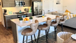 Une cuisine moderne dotée d’un îlot central, d’appareils électroménagers en acier inoxydable et de tabourets de bar.
