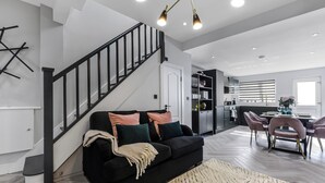 Ein modernes Wohnzimmer mit einem schwarzen Sofa, einer Treppe und einem Essbereich mit rosa Stühlen.