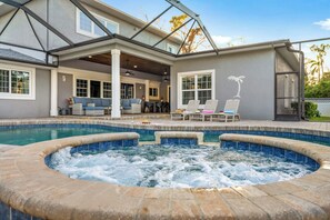 A swimming pool with a hot tub, outdoor seating, and a covered patio area.