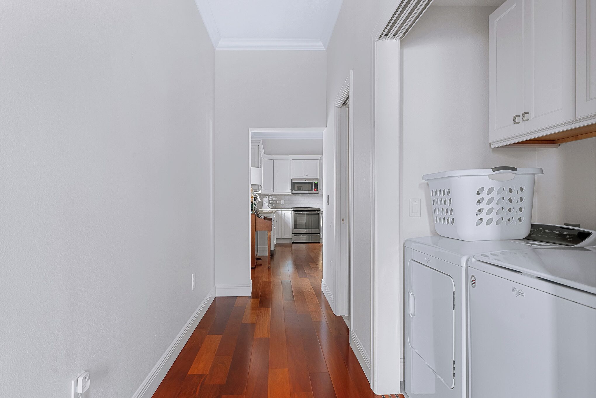 A narrow hallway with wooden flooring leading to a kitchen area with white cabinets and a microwave.