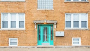 Un bâtiment de deux étages en briques, avec une porte turquoise, des fenêtres à cadre blanc et un petit auvent au-dessus de la porte.