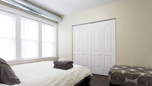 Une chambre à coucher avec un lit, une fenêtre, une armoire et un pouf à motifs.
