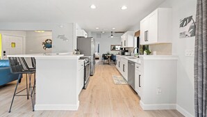 Cozinha moderna com armários brancos, uma ilha central e um espaço de refeições com uma cadeira azul.