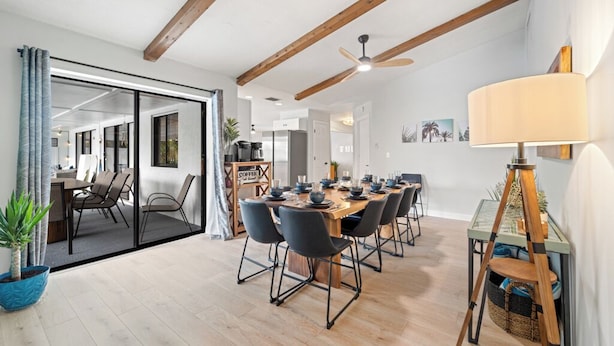 Uma sala de jantar moderna com mesa e cadeiras de madeira, um ventilador de teto e um espaço para café.