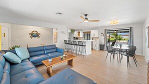 Uma sala de estar moderna com um sofá azul, uma mesa de centro de madeira e um espaço de refeições com cadeiras pretas.
