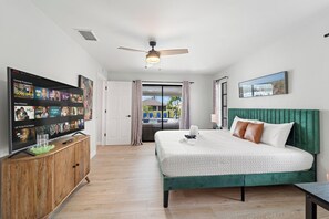 Habitación de hotel con una cama, un televisor sobre un mueble de madera, un ventilador de techo y vistas al exterior.