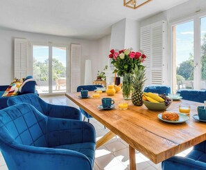 A bright dining area with a wooden table, blue chairs, and a view of the outdoors through large windows.