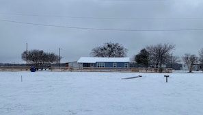 A snow-covered field with a building, a fence, and bare trees.