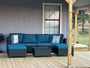 A covered porch with a sectional sofa, a fan, and a window.