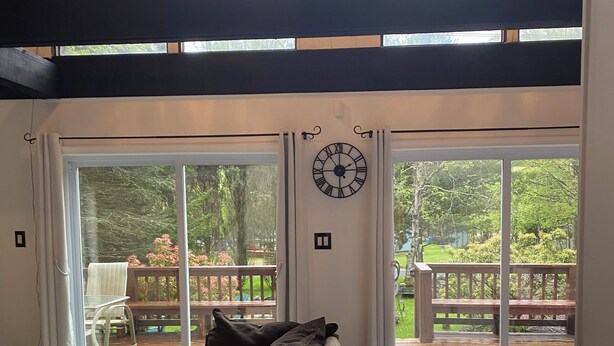 Un dormitorio moderno con una cama grande, un reloj en la pared y vistas a una terraza y jardín a través de puertas correderas de cristal.