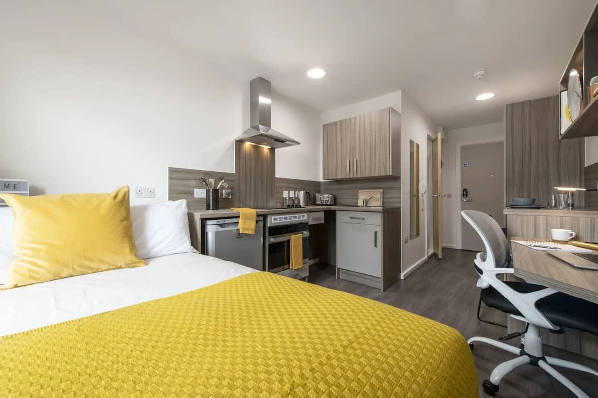 A compact hotel room with a bed, a desk, a kitchenette, and a bathroom.