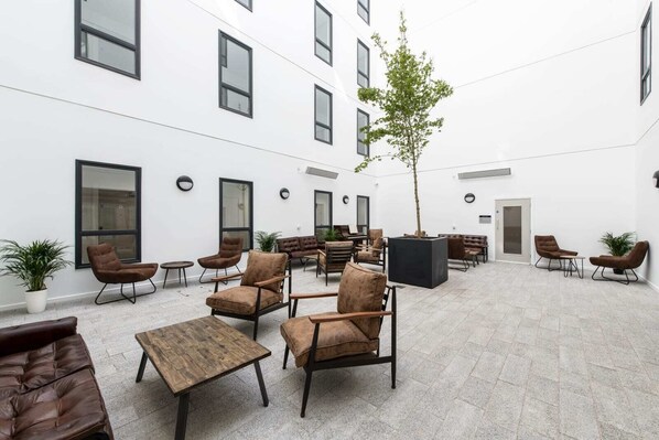 Un vaste espace extérieur aménagé avec plusieurs canapés et fauteuils, une table basse centrale et une plante en pot.