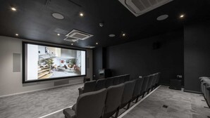 A modern cinema room with rows of grey seats, a large screen, and ceiling-mounted speakers. - Modern Apartments in Hollis Croft Sheffield (Sheffield)