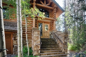 A log cabin with a stone staircase leading to a wooden door marked with the number 225.