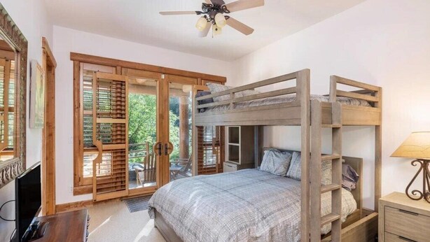 Ein Schlafzimmer mit Etagenbett, Holzmöbeln, Deckenventilator und einer Schiebetür zu einem Balkon.