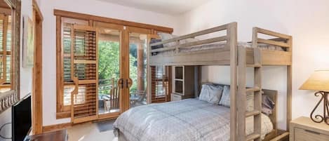 Ein Schlafzimmer mit Etagenbett, Holzmöbeln, Deckenventilator und einer Schiebetür zu einem Balkon.