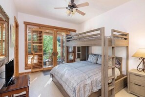 A bedroom with a bunk bed, wooden furniture, a ceiling fan, and a sliding glass door leading to a balcony.