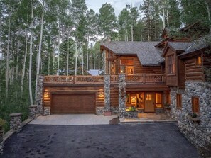 Une cabane en rondins avec des fondations en pierre, une terrasse en bois et un garage.