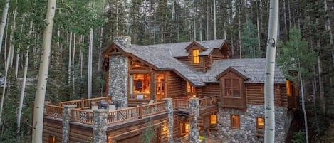 A log cabin with a stone foundation, multiple decks, and a stone chimney.