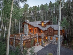 Une cabane en rondins avec des fondations en pierre, plusieurs terrasses et une cheminée en pierre.