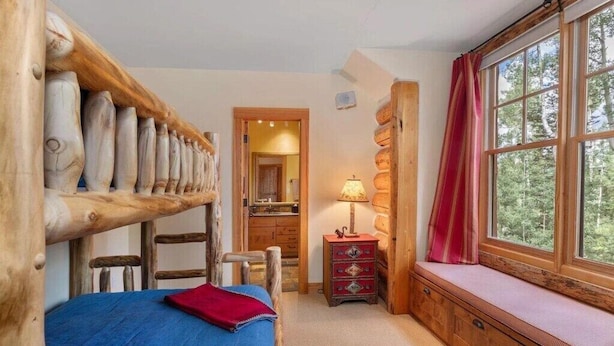 Una habitación rústica de madera con una cama, un banco con vistas y un pequeño aparador.