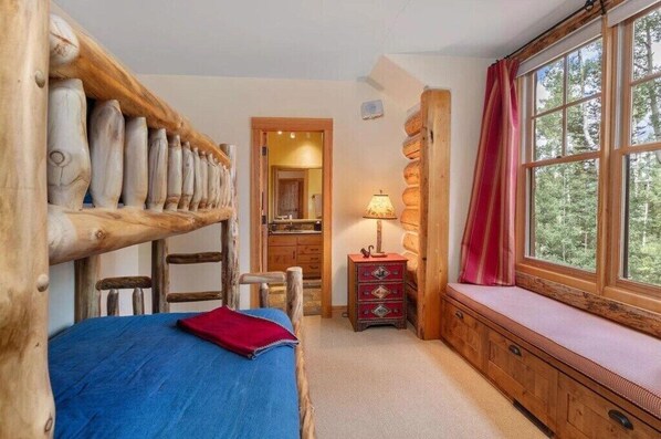 Une pièce rustique en bois, avec un lit, un banc offrant une belle vue et une petite commode.