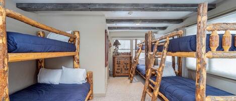 Una habitación con literas de madera natural, un pequeño aparador de madera y una ventana con vistas.