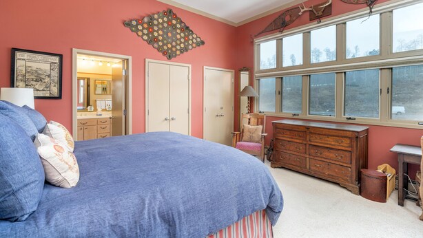 Un dormitorio con una cama grande, un tocador, un espejo y una ventana con vistas a árboles.