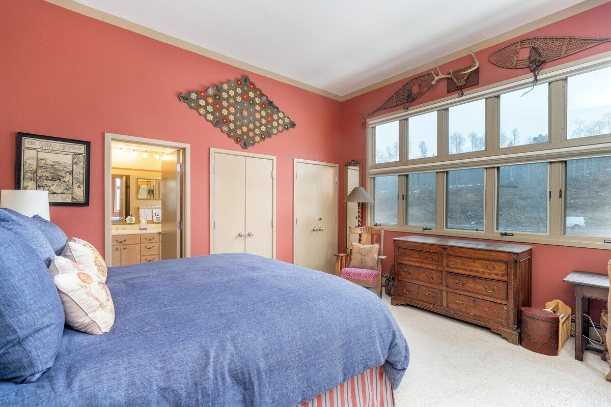 A bedroom with a large bed, a dresser, a mirror, and a window with a view.