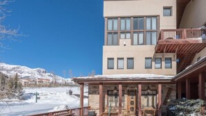 Un edificio a più piani con un balcone, un pontile in legno e vista su montagne innevate.