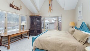 Een slaapkamer met een groot bed, een houten bankje, een donker houten kast en een ski-rek aan het plafond.