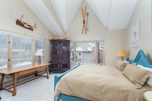 Une chambre avec un grand lit, un banc en bois, une armoire en bois foncé et un porte-skis fixé au plafond.