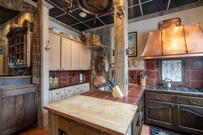A rustic kitchen with a wooden table, cabinets, and a copper range hood.