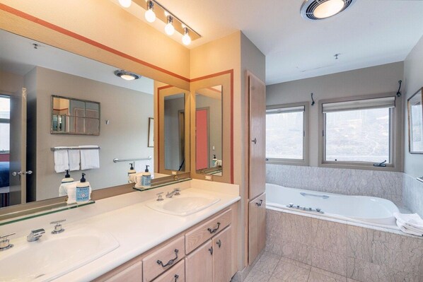A bathroom with a double sink, a large mirror, a bathtub, and a window.
