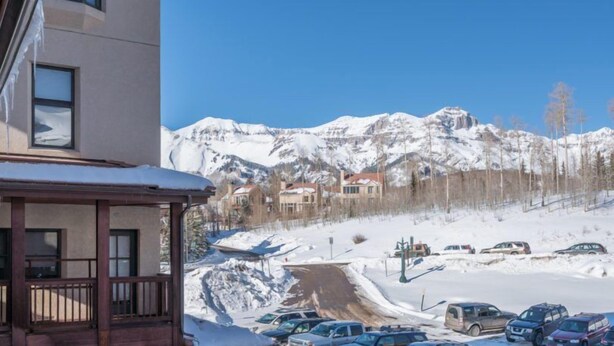 Een hotel met uitzicht op met sneeuw bedekte bergen en een parkeerplaats met meerdere auto's.