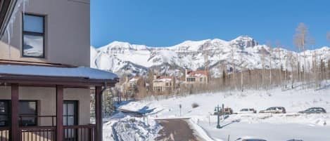 Un hôtel avec vue sur des montagnes enneigées et un parking où sont garées plusieurs voitures.