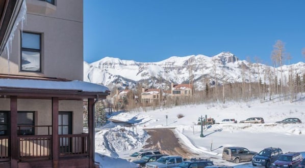 Un hôtel avec vue sur des montagnes enneigées et un parking où sont garées plusieurs voitures.