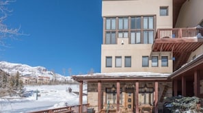 Un bâtiment doté d’un espace extérieur abrité avec des sièges, un paysage enneigé et des montagnes en arrière-plan.