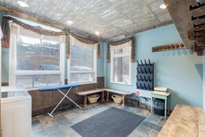 A laundry room with a bench, ironing board, and a drying rack.
