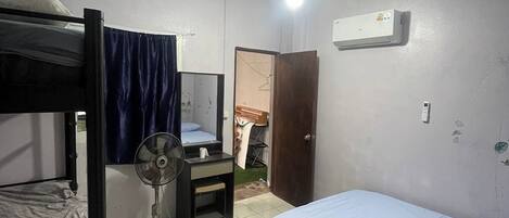 Habitación tipo dormitorio con literas, un escritorio, una silla, un ventilador y un equipo de aire acondicionado.
