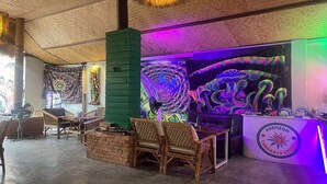 A room with a green pillar, wicker furniture, and a wall with psychedelic art. - Noah’s Ark Cannabis Bar Restaurant Hostel (Koh Samui)