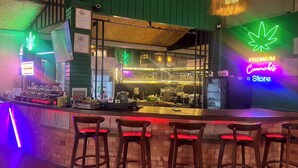 A bar area with a neon cannabis sign, a counter with stools, and a visible menu. - Noah’s Ark Cannabis Bar Restaurant Hostel (Koh Samui)