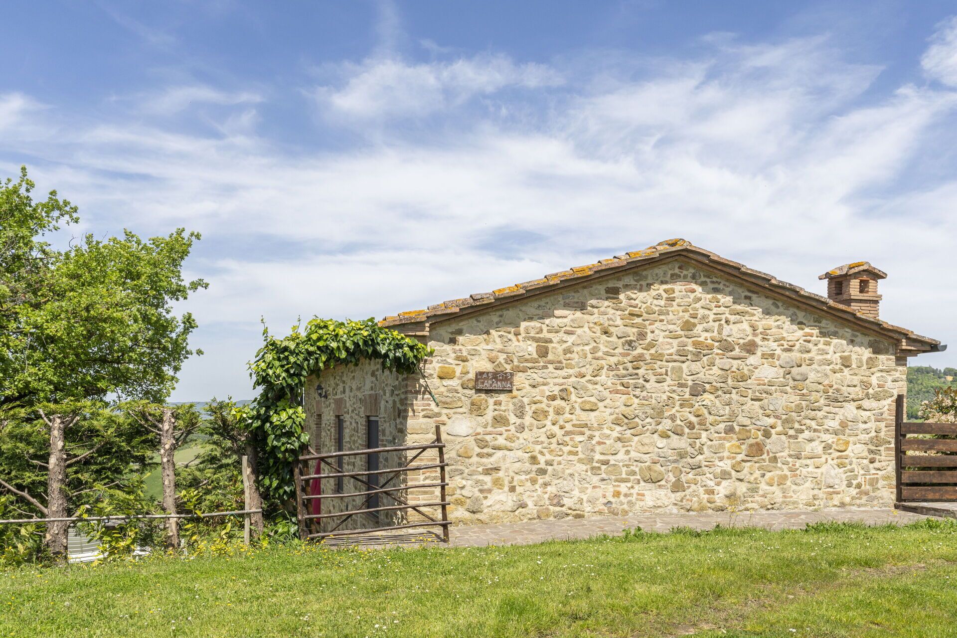 A stone building with a small attached structure, a metal gate, and a grassy area in front.