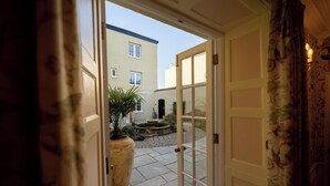 An open door leading to a courtyard with a large planter, a fountain, and a building in the background.