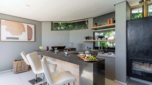 Eine moderne Küche mit einer zentralen Kochinsel, Barhocker, einem Kamin und einem großen Fenster.