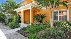A residential building with a covered porch, a well-maintained garden with various plants, and a clear sky. - Adorable townhome remodeled with comfort and relaxation in mind! Splash Pool! (Kissimmee)