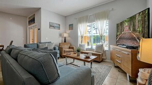 A living room with a sofa, armchair, coffee table, and a television on a wooden cabinet. - Adorable townhome remodeled with comfort and relaxation in mind! Splash Pool! (Kissimmee)