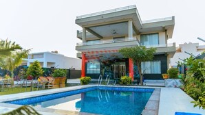 A modern two-story house with a swimming pool, outdoor seating, and a covered patio area.